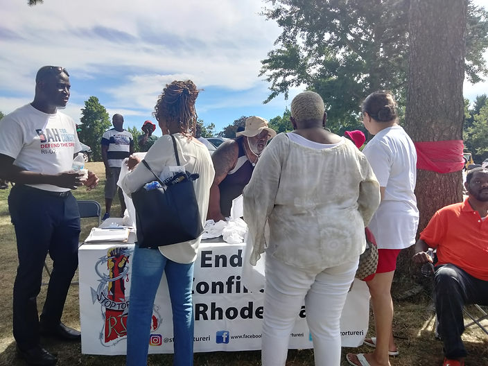 People gather around a table that has a banner that says, "End solitary confinement in Rhode Island." They are talking to each other